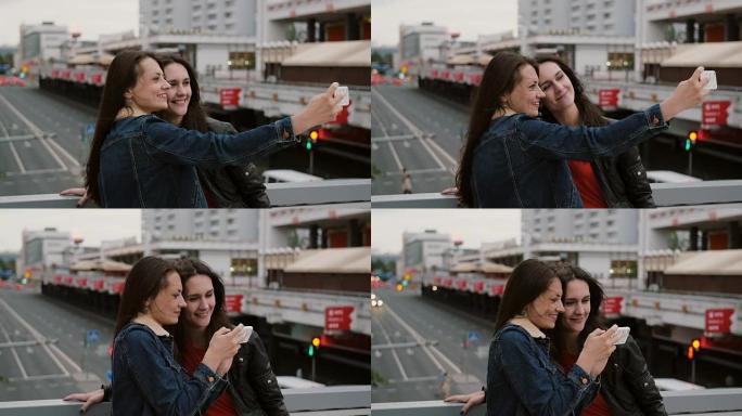 两个女孩最好的朋友自拍，站在城市的桥上，说话，微笑，大笑。全高清