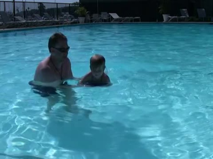 父亲教孩子游泳；浮在踢板上