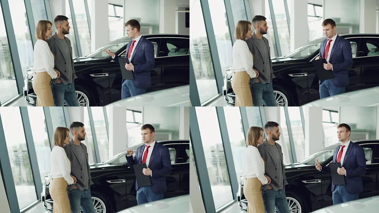 感兴趣的男女夫妇正在与汽车经销店的经理交谈，同时他正在向他们介绍豪华汽车模型。美丽的人，交通和商业理