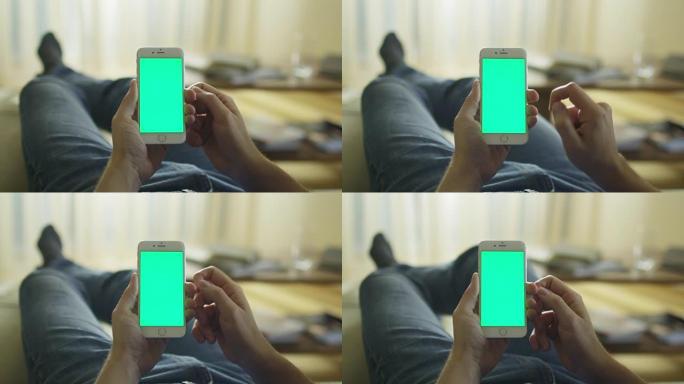 男人躺在家里的沙发上，在肖像模式下使用带有绿屏的电话。