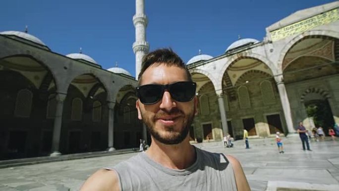 在伊斯坦布尔著名的蓝色清真寺附近使用智能手机摄像头进行在线视频聊天的快乐旅游男子的手持设备