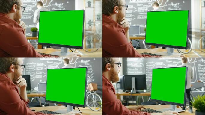 Man在带有绿色模拟屏幕的个人计算机上工作。在背景创意办公室，男人在黑板墙上画画。