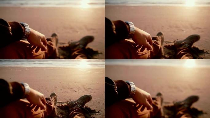 一个男人坐在沙滩上穿着靴子看着美丽的日落的第一视点视频