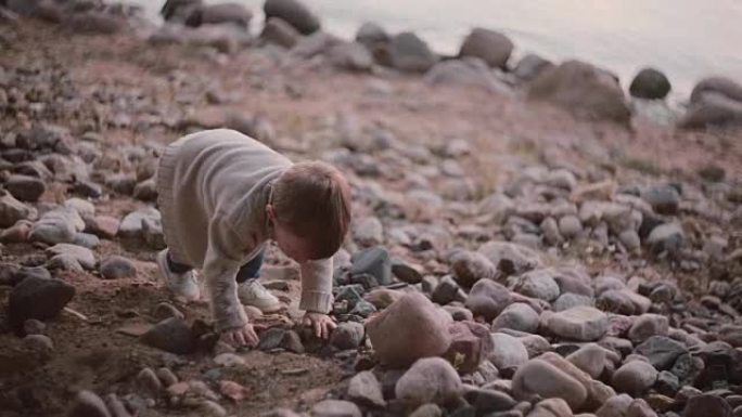 可爱的小男孩走过石头靠近水。雄性落在岩石上并上升