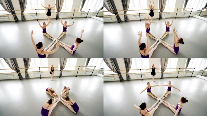勤奋的小芭蕾舞演员在芭蕾舞老师的指导下坐在工作室的地板上伸展和移动手臂，练习向前弯曲的高角度视图。
