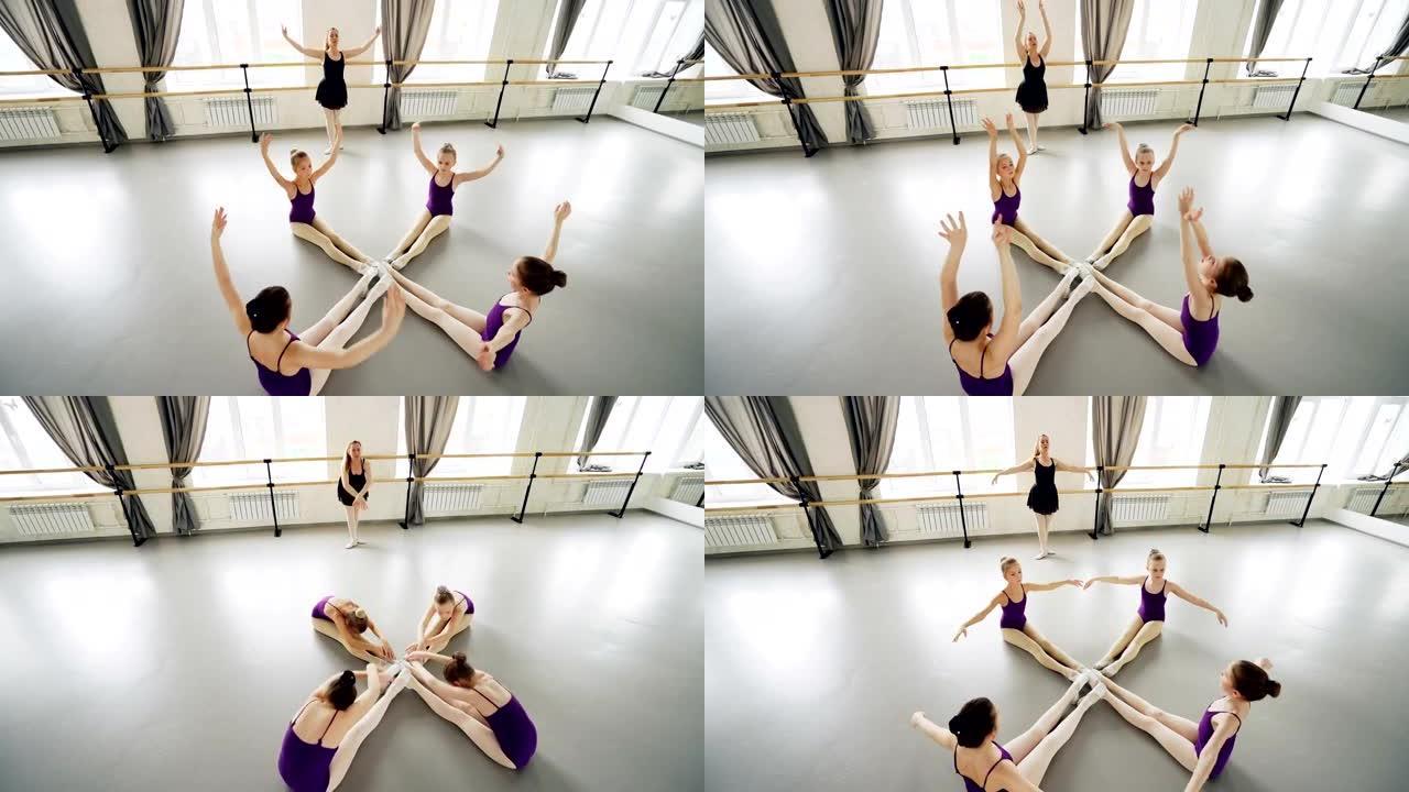 勤奋的小芭蕾舞演员在芭蕾舞老师的指导下坐在工作室的地板上伸展和移动手臂，练习向前弯曲的高角度视图。