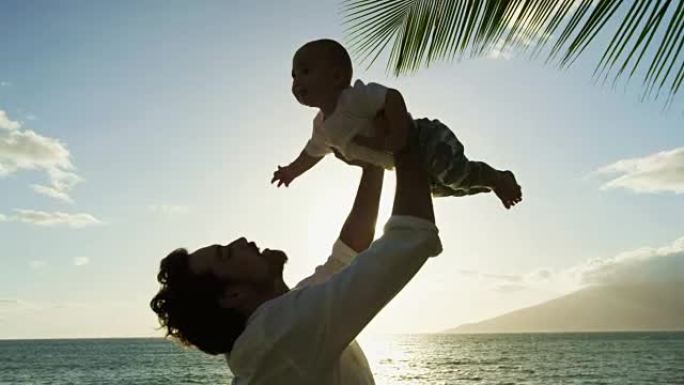 年轻的爸爸在日落时以慢动作举起婴儿