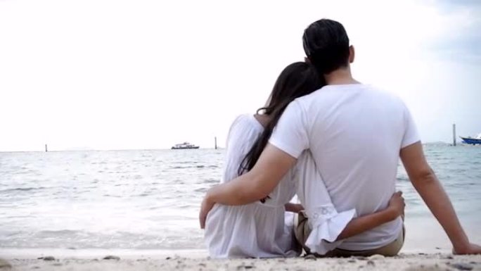浪漫的情侣坐在沙滩上享受日落，拥抱第一次散焦。