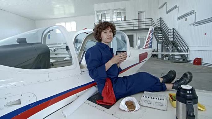 女飞机机械师在机库吃午餐时喝茶