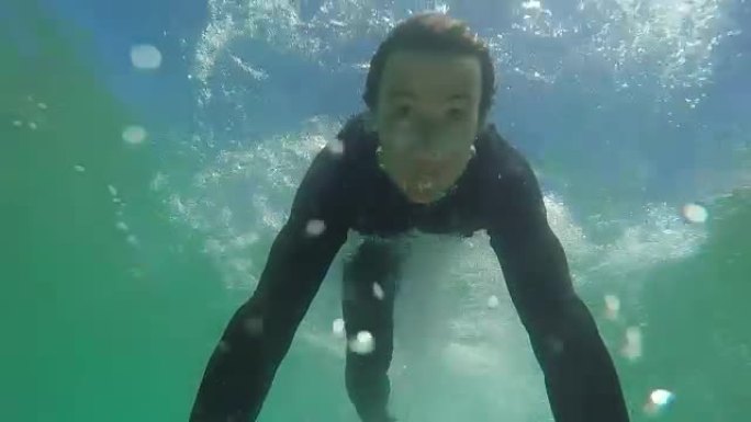 慢动作特写: 快乐的年轻冲浪者鸭子在海浪下潜水