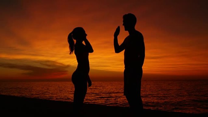 慢动作，剪影: 日落时分，年轻男女在海边击掌。