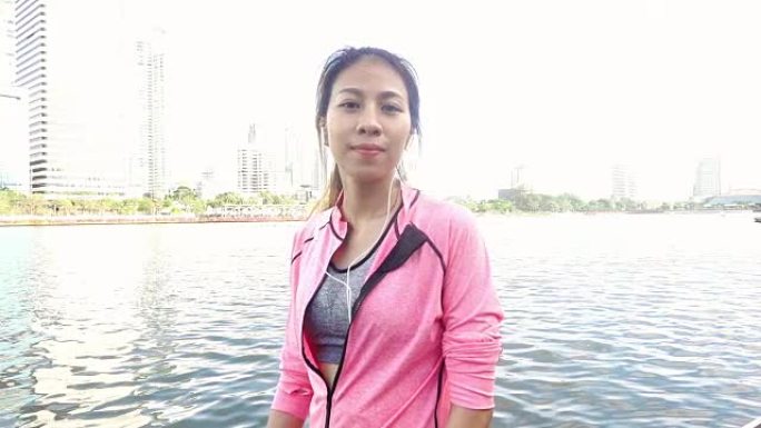 慢动作-穿着健身服装的亚洲美女正在使用智能手表听音乐，在公园跑步后打电话。迷人的健康女性慢跑。