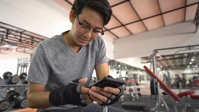 亚洲男子在密集的交叉健身健美健身房训练后，在长凳上休息时使用智能手机拍摄了2张照片