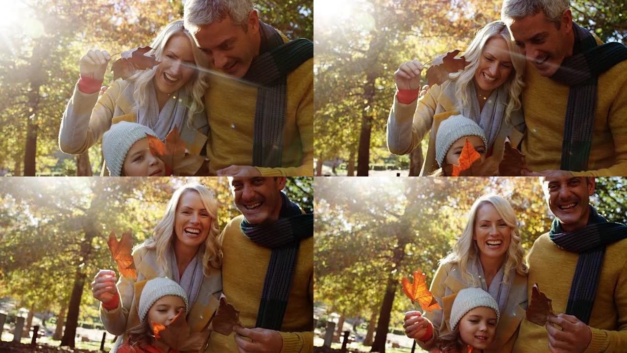 爸爸妈妈和女儿拿着树叶在户外微笑