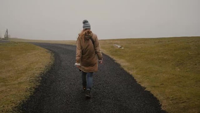 年轻女子独自走过田野的后景。探索冰岛自然的时尚女性