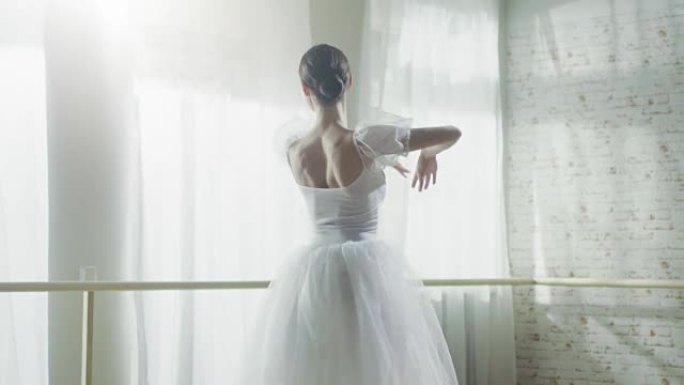 年轻美丽的芭蕾舞演员在她的尖头芭蕾舞鞋上优雅地跳舞。她穿着白色短裙。工作室阳光明媚，现代。慢动作。