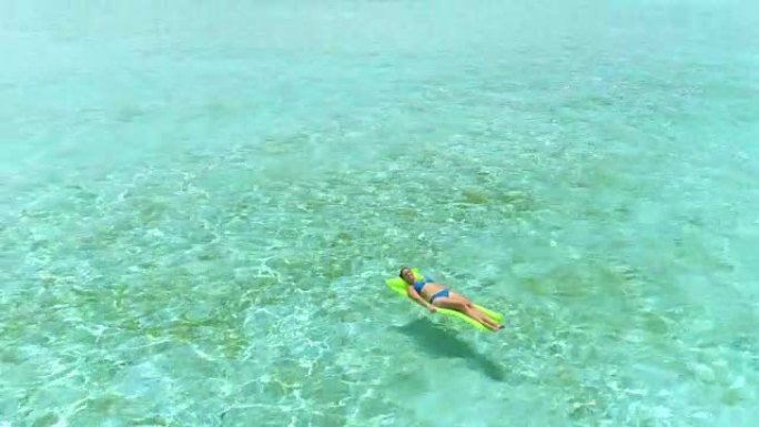 空中: 年轻女子在波拉波拉 (Bora Bora) 的阳光明媚的假期中，在浮动气垫床垫上放松身心