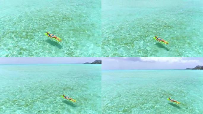 空中: 年轻女子在波拉波拉 (Bora Bora) 的阳光明媚的假期中，在浮动气垫床垫上放松身心