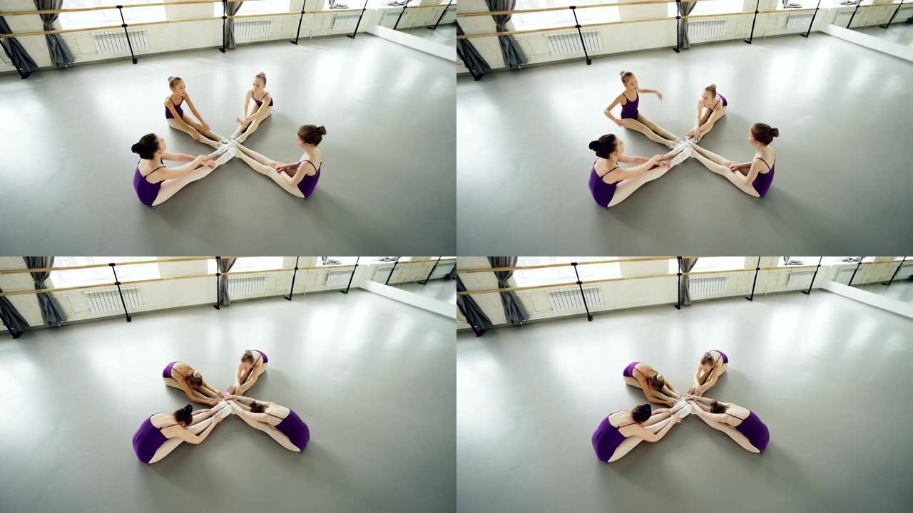 灵活的芭蕾舞演员的高角度视图，他们从头到膝盖弯曲，坐在工作室的地板上伸展腿和背部。编排、灵活性和计时