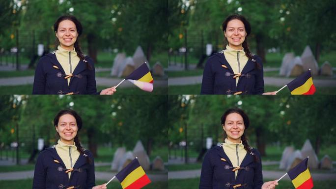 穿着便服的漂亮女孩的慢动作肖像，微笑着挥舞着比利时国旗，高兴地看着相机。年轻女性，快乐公民，欧洲国家