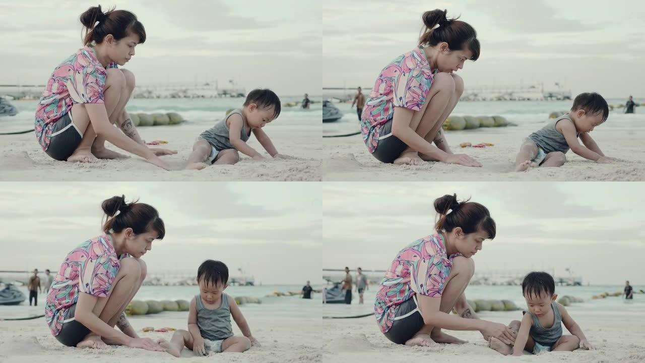 年轻的亚洲母亲和小男孩在沙滩上玩沙子。