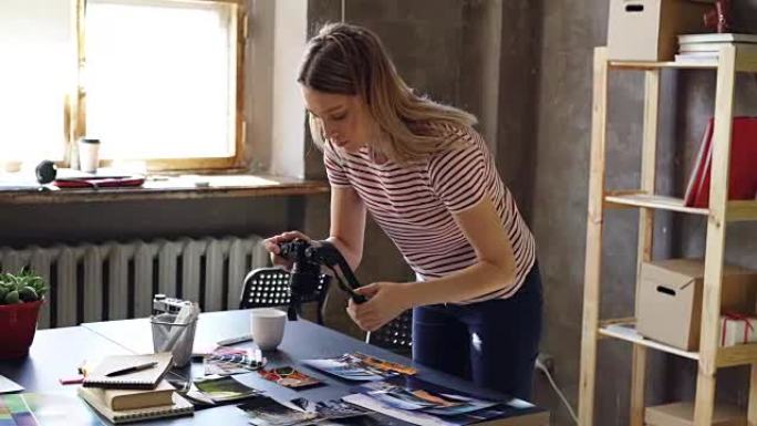年轻迷人的女性博客作者使用数码相机拍摄桌上展示的旅行照片。她正在移动照片和制作拼贴画。