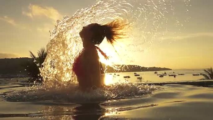 慢动作: 顽皮的年轻女子在日落时将头发从无边泳池中抽出。