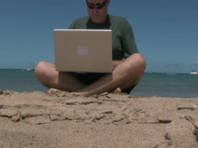 工作狂男子在海滩度假时使用笔记本电脑