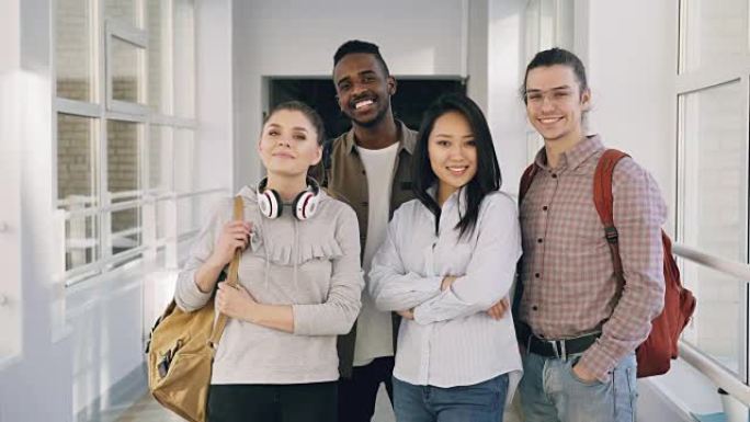 四名微笑的积极有吸引力的多民族男女学生的肖像站在大学宽敞的白色走廊上看着相机