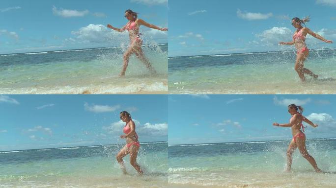 慢动作: 穿着粉红色比基尼的快乐女孩在海滩边奔跑，溅水。
