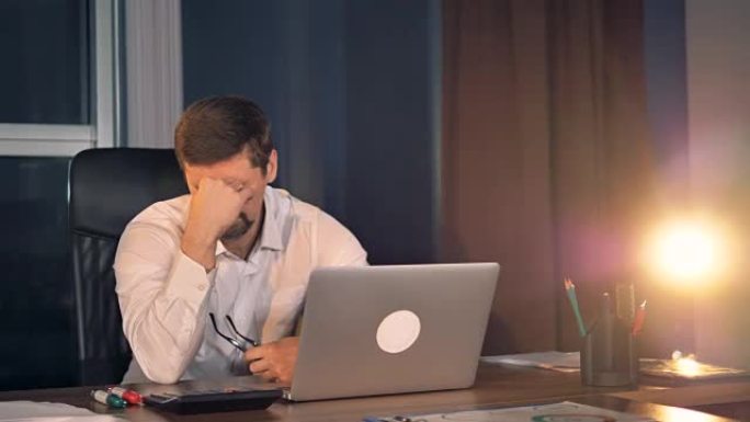 一个昏昏欲睡的商人在笔记本电脑上工作到很晚。