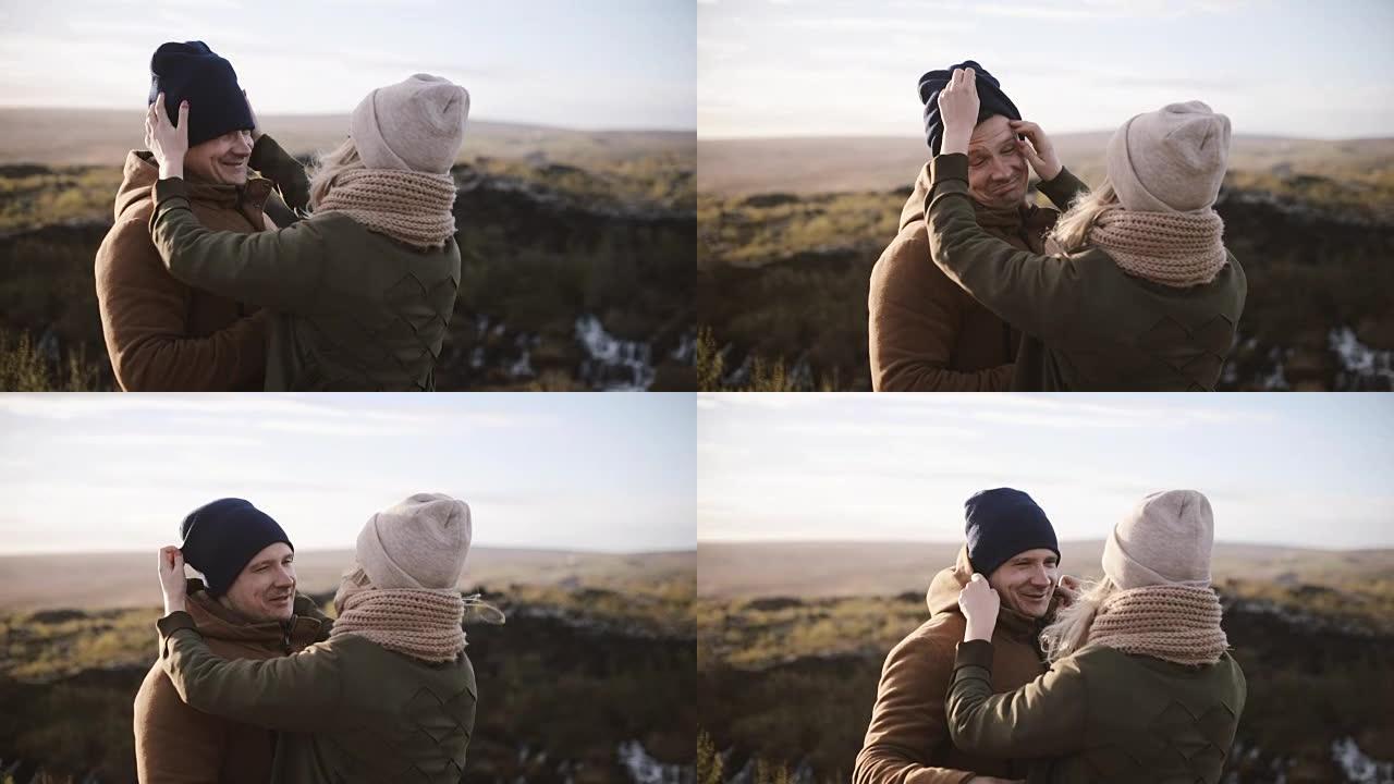 年轻美丽的夫妇一起享受大自然的乐趣。女人戴上男人的帽子，在大风天笑
