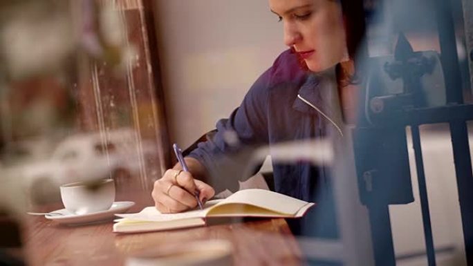 年轻女子在咖啡店的靠窗座位上写日记
