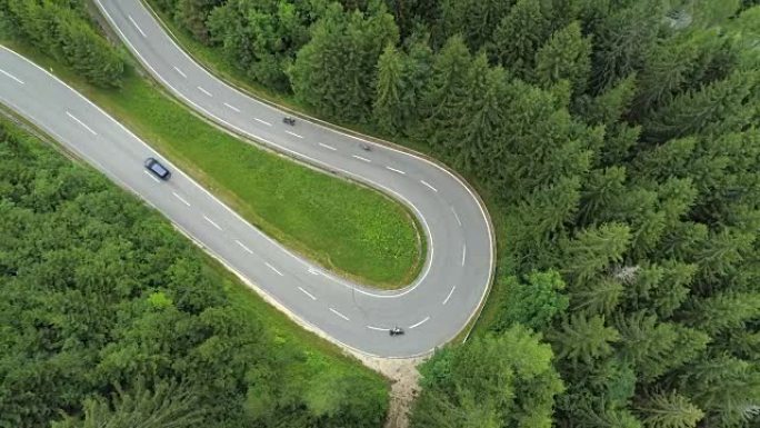 空中: 摩托车和汽车在起伏的道路上驶过发夹弯