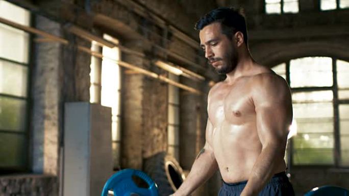 肌肉裸男用力举起沉重的杠铃，在工业健身房做二头肌弯曲/健身运动。