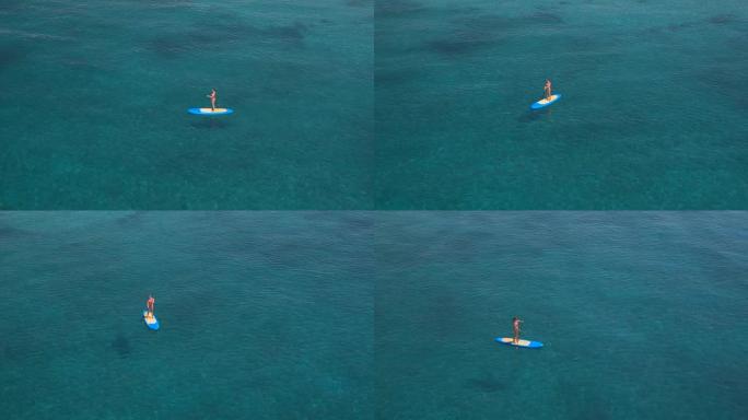 空中: 活跃的年轻女冲浪者在热带海洋中站立划板