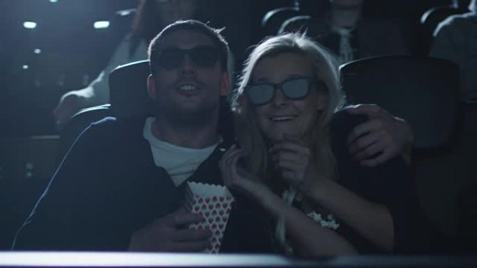 在电影院里有趣的5d电影放映中，当爆米花被从盒子里摇出来时，夫妻俩互相拥抱。