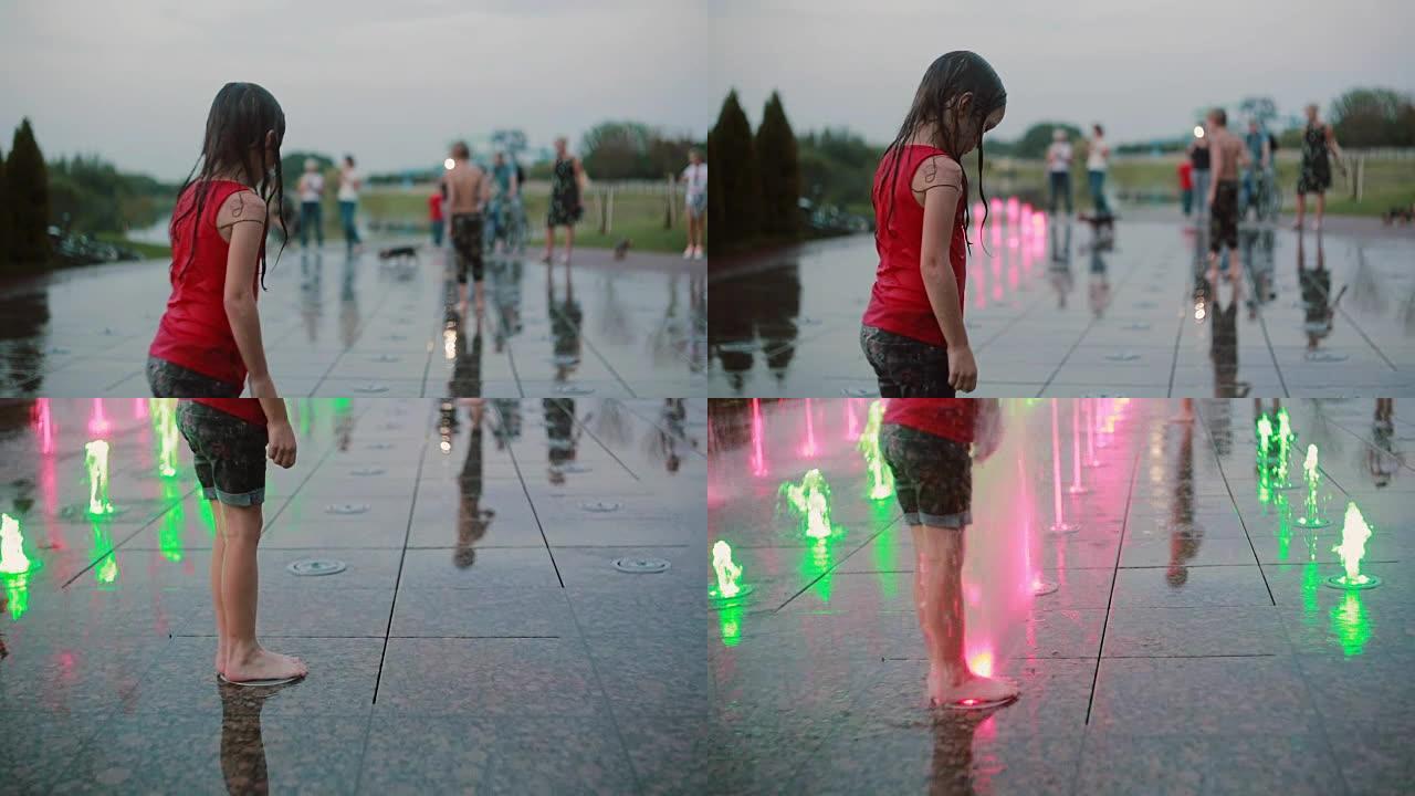 湿的小女孩站在玩水，站在喷泉喷射上。快乐的孩子在炎热的夏天玩得开心