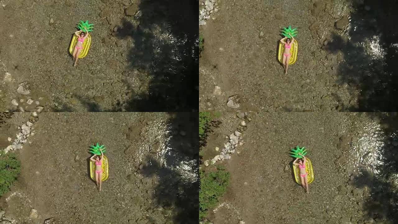 炎热的夏日，空中年轻女子在菠萝漂浮物上滑下河
