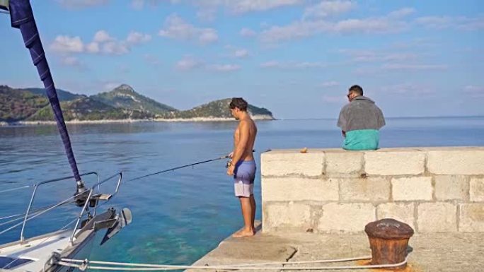 4k年轻人在阳光明媚的海洋上的岩壁上钓鱼