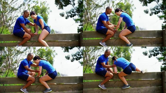 男性教练协助健康女性在障碍路线4k时爬过木墙