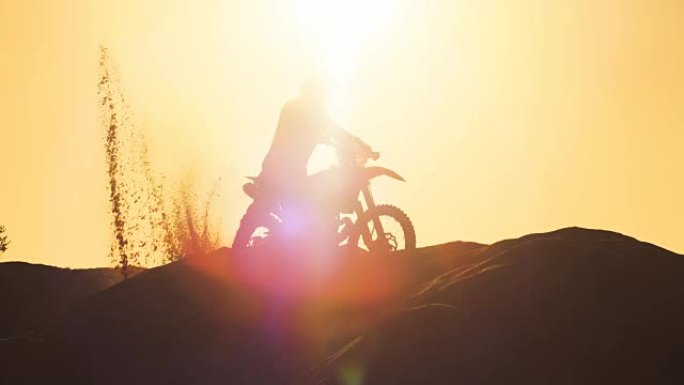 职业摩托车越野者在FMX摩托车上做Wheelie沙丘和骑下车。他的剪影是可见的日落在背景。