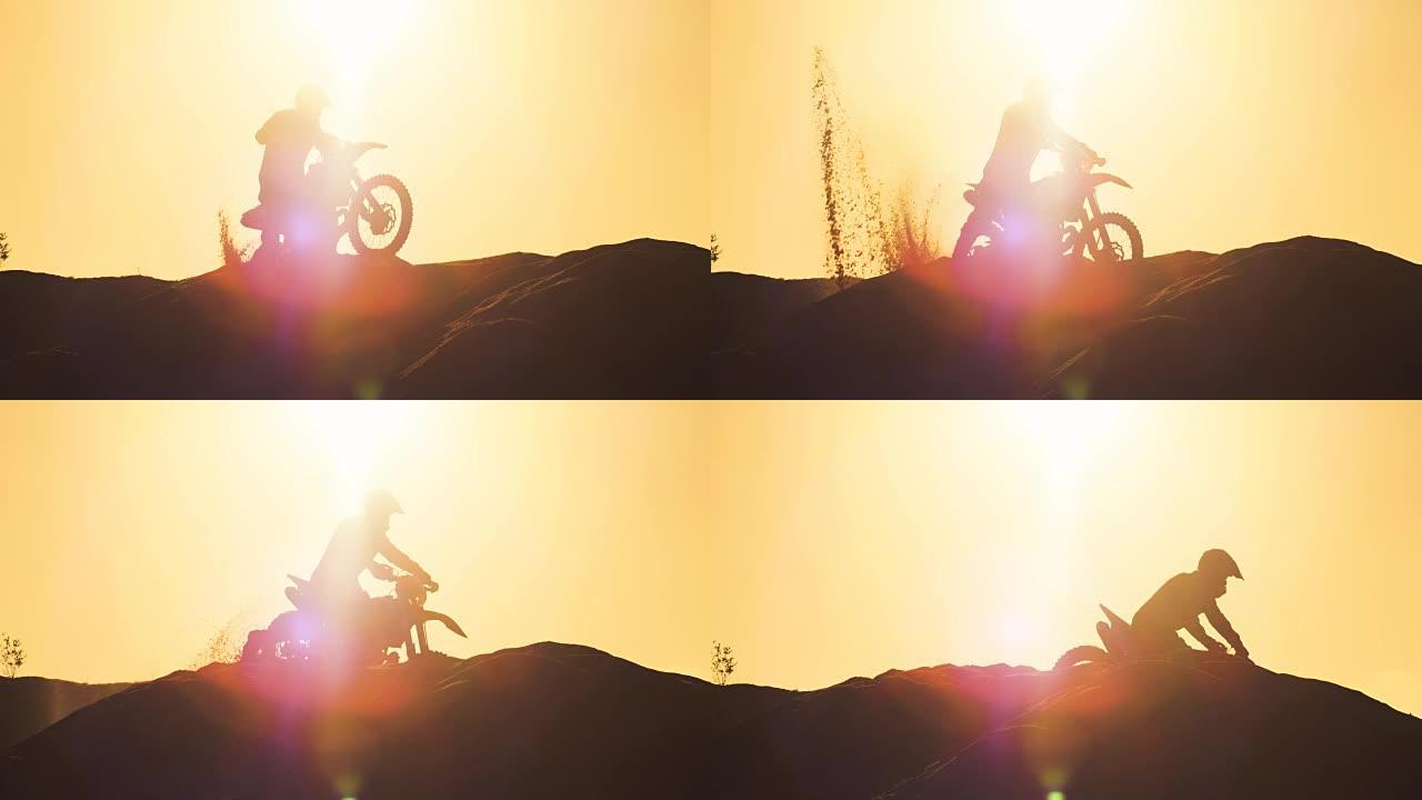 职业摩托车越野者在FMX摩托车上做Wheelie沙丘和骑下车。他的剪影是可见的日落在背景。