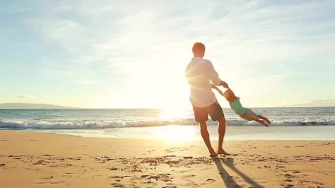 年轻的父亲在日落时与儿子在海滩上玩耍。转圈。
