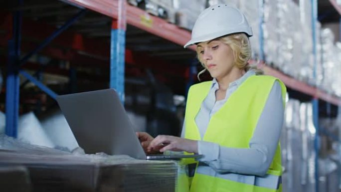 物流仓库的女工正在笔记本电脑上工作。戴着白色安全帽。
