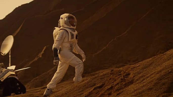 宇航员登上高山探索红色星球/火星。背景:他的基地和人工智能驱动的漫游车。未来殖民的概念。