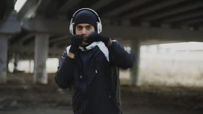冬季在户外城市位置进行拳击运动的耳机运动男子拳击手的跟踪镜头