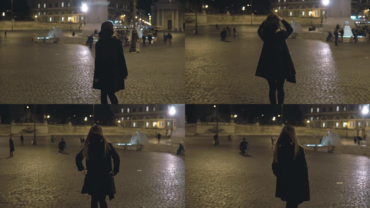 年轻女子独自走在夜城。迷人的女性在市中心的广场上等着某人