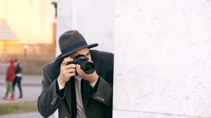 年轻的男性间谍戴着帽子和外套拍摄罪犯和躲在墙后面