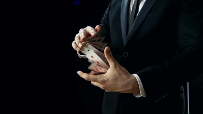 魔术师双手表演纸牌戏法的特写镜头。在空中投掷和捕捉纸牌。背景是黑色的。慢动作。
